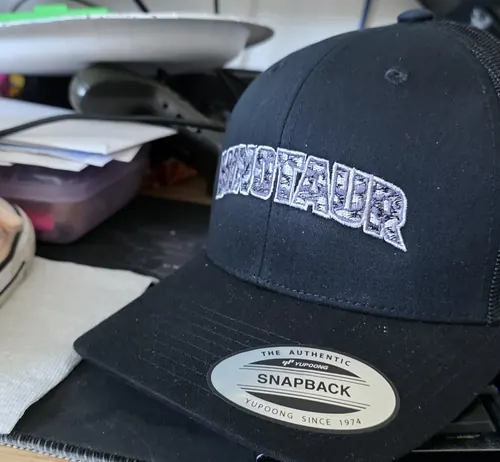 Black trucker cap with an arched Minotaur wordmark on the front and a bull logo on the side