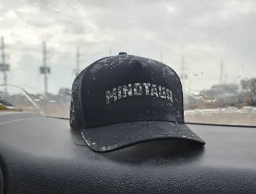 Black cap with a tonal Minotaur wordmark, photographed on a car dashboard